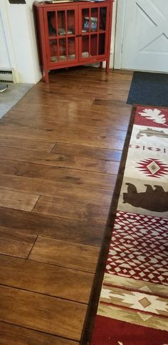 a wooden floor with a red cabinet and rug on the ground in front of it