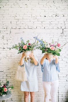 two women are holding flowers in front of their faces while standing against a white brick wall