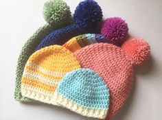 four crocheted hats with multi colored pom - poms sitting on top of each other