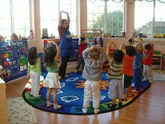 a group of children standing on top of a blue rug in a room with windows