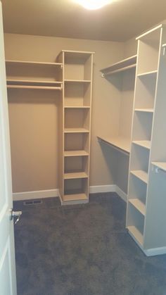 an empty walk in closet with white shelving and gray carpeted flooring is shown