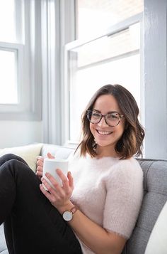 a woman sitting on a couch holding a coffee cup in her hand and smiling at the camera