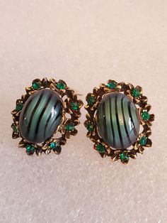 "These Art Nouveau clip On's are from the 1950's made out of a brass base metal in an oval shape with flowers surrounding the raised center. At the center a large dome shaped glass cabochon in a hunter green with black stripes. These are your classic MADMAN earrings. They are in excellent vintage condition with no hallmark. They came from an Estate Sale in Louisville, Co. They will arrive in a gift box with FREE SHIPPING. Measures: 1\"L X 1\"W Material: Brass base metal and clips, green rhinesto Vintage Oval Earrings For Evening, Vintage Green Cabochon Earrings, Victorian Metal Clip-on Earrings, Victorian Style Metal Clip-on Earrings, Vintage Oval Pierced Earrings, Vintage Metal Cabochon Earrings, Vintage Cabochon Earrings For Evening, Vintage Cabochon Metal Earrings, Vintage Cabochon Clip-on Earrings