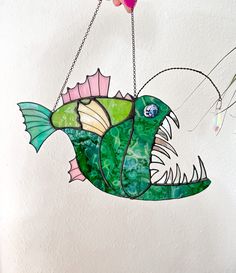 a stained glass fish hanging from a chain on the wall next to some flowers and beads