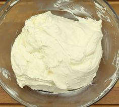 a glass bowl filled with white frosting on top of a wooden table