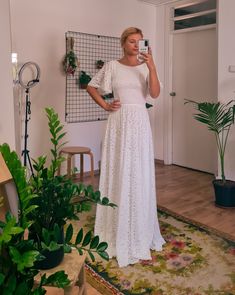 a woman in a white dress taking a selfie with her cell phone while standing next to plants