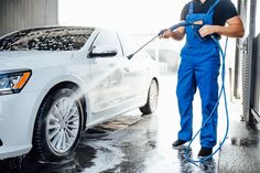 a man in blue overalls washing a white car with a high pressure washer