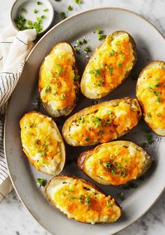 baked potatoes with cheese and chives in a plate on a marble countertop next to a napkin