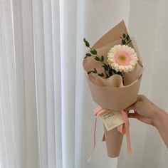 a person holding a bouquet of flowers in front of a white curtain with pink ribbon