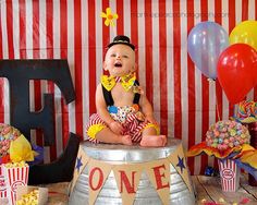 a baby sitting on top of a bucket filled with popcorn next to balloons and streamers