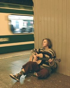 a woman sitting on the ground with a guitar in front of her and a train passing by