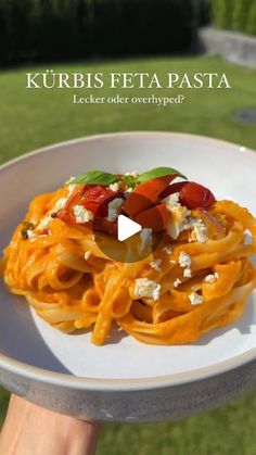 a white plate topped with pasta covered in cheese and tomato sauce on top of a green lawn