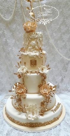 a three tiered white and gold wedding cake with flowers on the top, sitting on a lace covered tablecloth