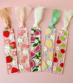 four bookmarks with fruit and flowers on them, lined up against a pink background