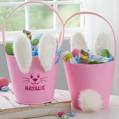 two pink buckets filled with candies and marshmallows on top of a wooden table