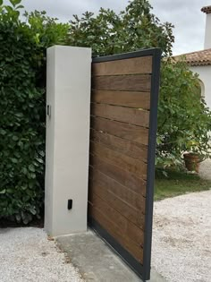 an open wooden door in front of a white house with green bushes and trees behind it