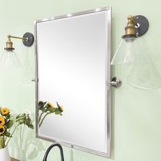 a bathroom mirror sitting on top of a wall next to a vase with flowers