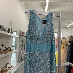 a blue dress hanging on a rack in a clothing store with shoes and handbags