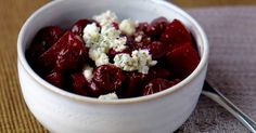 a white bowl filled with beets and cheese on top of a brown place mat