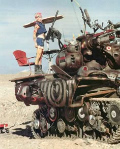 a man standing on top of a tank made out of old cars and other junk