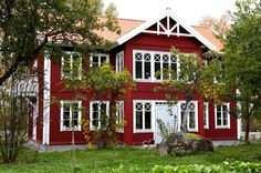 a red house with white trim on the front and windows is surrounded by greenery