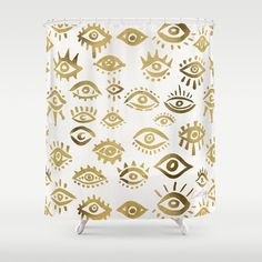 gold and white shower curtain with an all seeing eye pattern on the bottom, in front of a gray background