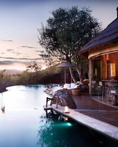 an outdoor swimming pool at dusk with lounge chairs and umbrellas on the deck next to it