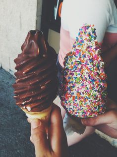 two ice cream cones with sprinkles are being held by someone's hand