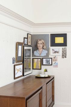 a wooden dresser sitting next to a wall covered in pictures and framed art on it