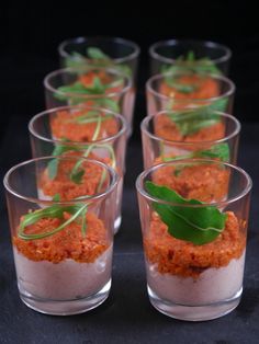 small glasses filled with food sitting on top of a table next to each other and garnished with green leaves