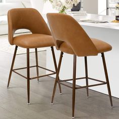 two brown leather bar stools sitting in front of a white counter top with flowers on it