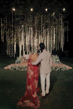 a man and woman standing in front of a tree with white lights hanging from it