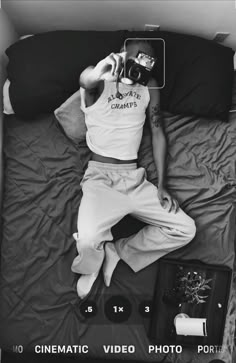 a man laying in bed taking a photo with his camera and some other items around him