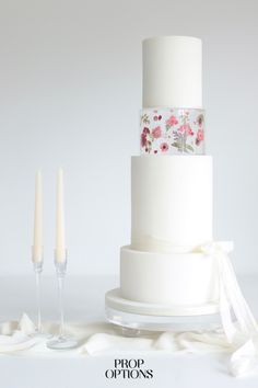 a three tiered white wedding cake with pink flowers on it and two candles next to it