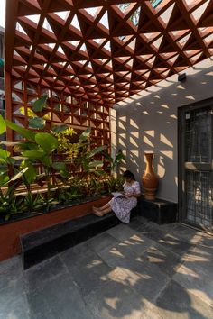 a woman sitting on the ground in front of a building with a wooden structure above her