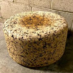 a large round stool sitting on top of a cement floor next to a brick wall