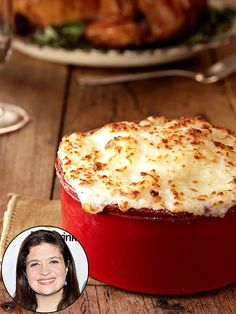 a red casserole dish sitting on top of a wooden table next to a glass of wine