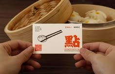 two hands holding up a business card with chopsticks in front of some food