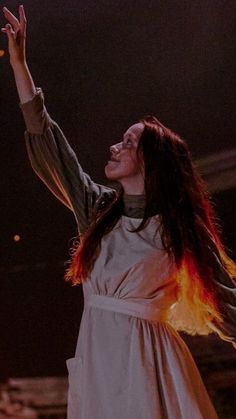 a woman with long hair wearing a white dress and holding her arms up in the air