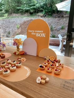 there are cupcakes on the table with an orange sign in the background that says here comes the son