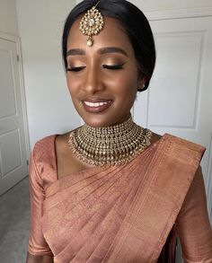 a woman in an orange sari with gold jewelry on her neck and chest is smiling