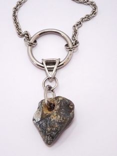 The necklace is made of a decorative silver chain. In the middle there is a metal circle with a diameter of 3 cm, a metal element connected to a natural stone of irregular shape. There is one hole in the stone, gray with a touch of beige. The stone comes from a beach in southern England. In Celtic culture, stones with holes, the so-called The Hag Stone or Odin Stone were good luck amulets that protected against negative energy.  The stone measures 3.3 x 2.6 cm.  A unique gift, unisex. Metal Necklaces With Natural Stones And Round Pendant, Metal Necklace With Round Pendant And Natural Stones, Silver Necklace With Large Oval Pendant, Spiritual Metal Necklaces With Natural Stones, Spiritual Metal Necklace With Natural Stones, Round Gemstone Metal Necklace, Unique Silver Circular Necklace, Unique Silver Necklace With Raw Stone, Metal Necklaces With Natural Stones For Healing