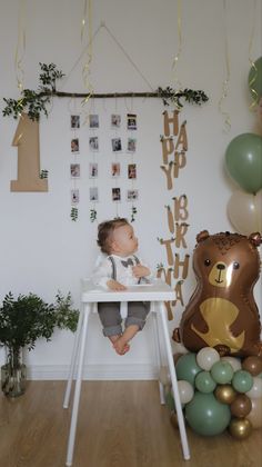 a baby is sitting in a high chair with balloons and decorations around him on the wall