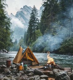 a tent is set up on the bank of a river with a campfire in front of it