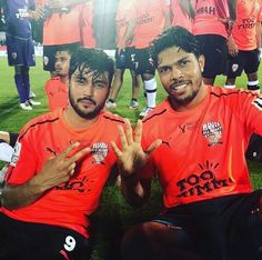 two soccer players sitting on the ground with their hands up in front of them, posing for a team photo