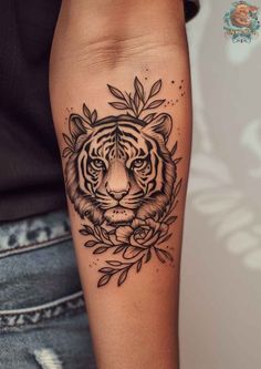 a black and white tiger tattoo on the arm, with leaves around its head in front of