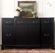 a black sideboard with two vases on top and a painting hanging above it