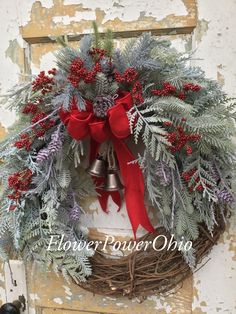 a christmas wreath with bells and evergreens hanging on an old wooden door, decorated with red ribbon