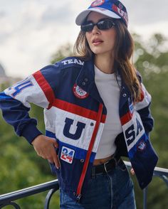 a woman in a baseball cap and jacket standing on a balcony with her hands on her hips