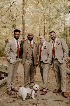 three men in suits and one dog pose for the camera while standing on a bridge